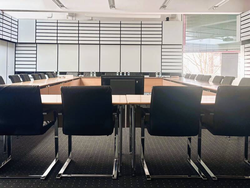 Ein großer moderner Konferenzraum mit einem rechteckigen Tisch und vielen schwarzen Stühlen in einem hellen Raum.