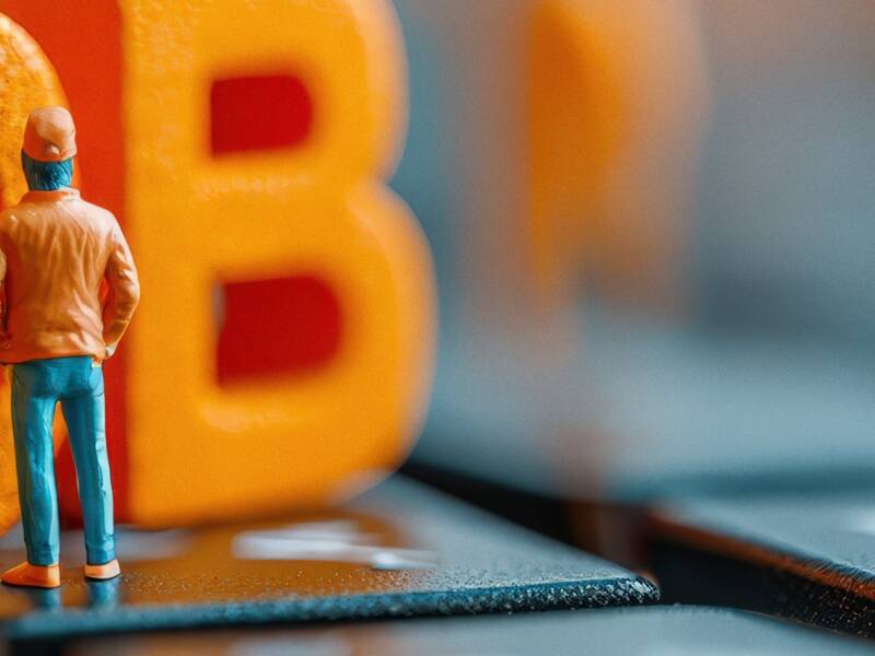 Eine kleine Figur steht vor überdimensionalen orangefarbenen Buchstaben, die das Wort "JOB" bilden, auf einer Computertastatur.