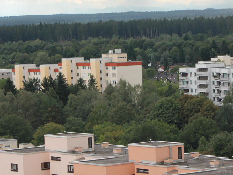 verscheidenfarbige Hochhäuser umgeben von Wald mit bewölktem Himmel