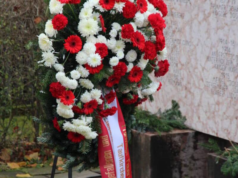 Ein mit rot und weiß geflochtener Kranz mit einer rot weiß rot gestreiften Schleife stehen vor dem Kriegerdenkmal
