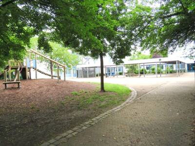 Klettergerüst umgeben von Bäumen steht im Pausenhof der Grundschule
