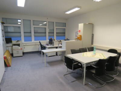 Blick in ein Büro mit zwei Schreibtischen und einem Besprechungstisch mit schwarzen Stühlen